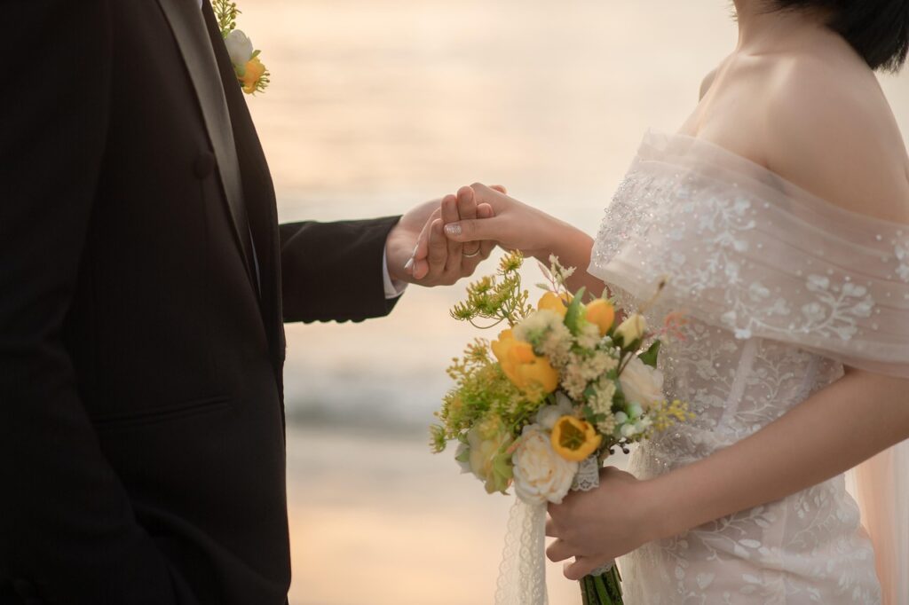 花嫁と花婿が海辺で手を取り合っている写真。