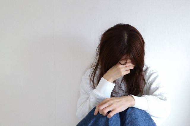 女性が、体調がすぐれず、座ってうつむいている写真。